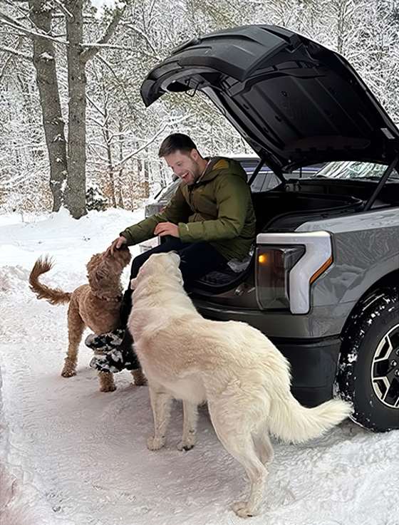 Cyril Brunner sits on the frunk of his Ford F-150 Lightning with his dogs, Tucker and Dexter
